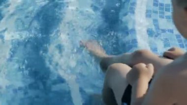Çocuk Havuzu kenarında oturan ve bacakları su sıçramasına tekme
