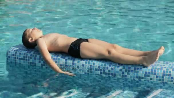 リラックスできるプールサイド近くの少年 — ストック動画