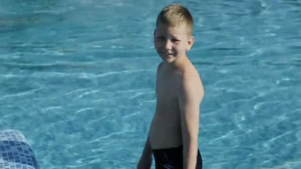 Niño en traje de baño negro salta a la piscina azul — Vídeo de stock