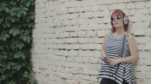 Κοκκινομάλλης γυναίκα από τον τοίχο που φορούν ακουστικά — Αρχείο Βίντεο