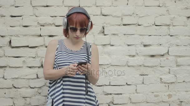 Red-haired 妇女在墙壁听音乐在耳机 — 图库视频影像
