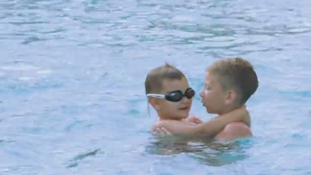 O menino ensina o bebê a fechar o nariz e mergulhar na piscina — Vídeo de Stock