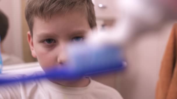 Young boy squeezes toothpaste on toothbrush and brushes teeth — Stock Video
