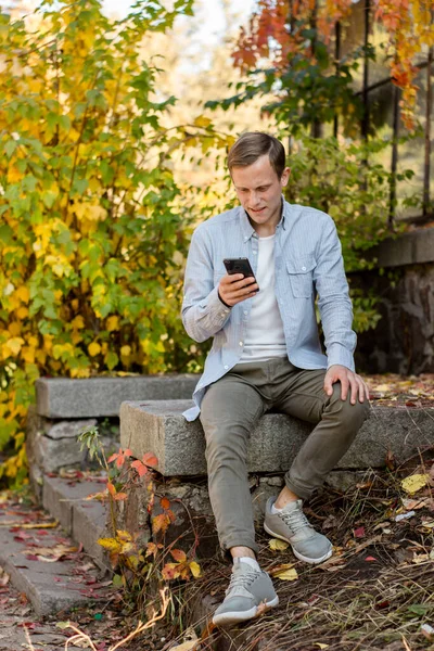 Guy with a phone in casual clothes in the autumn park