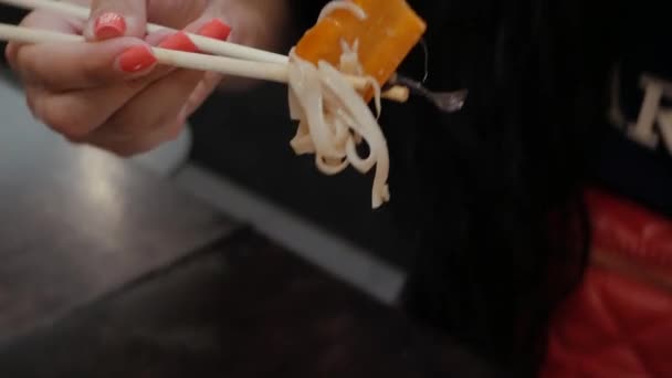 Молодая женщина ест палочки для еды лапшу — стоковое видео