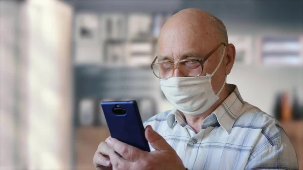 Old man reading news from a smartphone at home