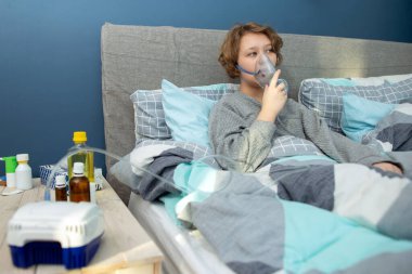 teenager girl doing inhalation indoor , Young woman doing inhalation with a nebulizer at home clipart