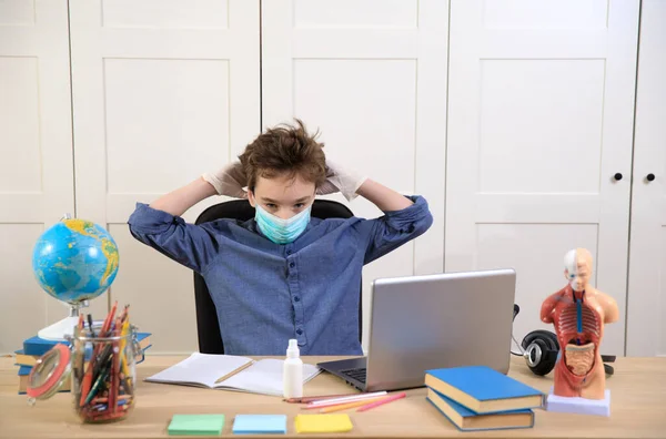 Distance learning online education. schoolboy in medical mask studying at home, coronavirus quarantine