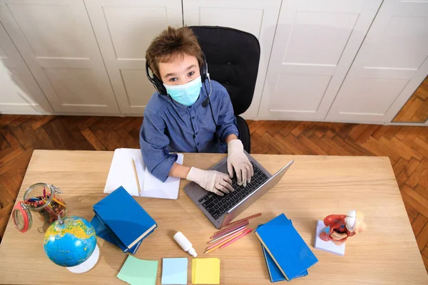 遠隔オンライン教育 家庭で勉強している医療用マスクの少年コロナウイルスの隔離 — ストック写真
