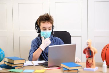 Uzaktan öğrenme çevrimiçi eğitim. Tıp maskeli çocuk evde ders çalışıyor. Coronavirus karantinası.