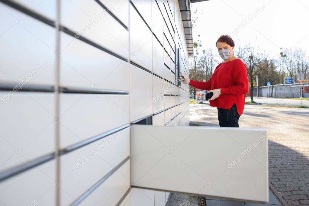 A woman in protective mask and medical gloves using an automatic self-service terminal or a locker to pick up, deposit a package for storage. Quarantine delivery, outbreak, covid-19 coronavirus in a pandemic, safety delivery