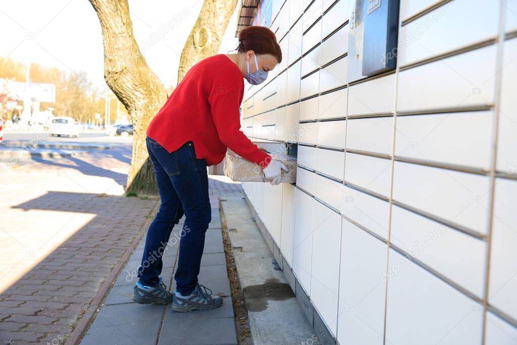 A woman in protective mask and medical gloves using an automatic self-service terminal or a locker to pick up, deposit a package for storage. Quarantine delivery, outbreak, covid-19 coronavirus in a pandemic, safety delivery