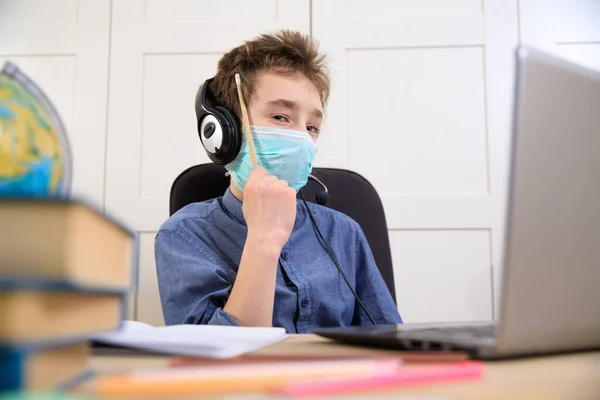 Distance learning online education. schoolboy in medical mask studying at home, working at laptop notebook and doing school homework. coronavirus quarantine