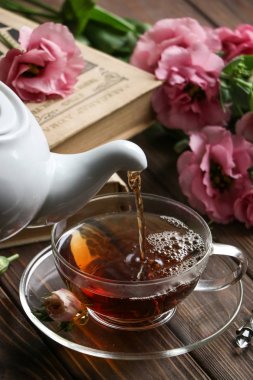 sabah natürmort pembe eustoma çiçekler, iki bej eski kitaplar ve cam bardakta ahşap masa bir sıcak siyah çay