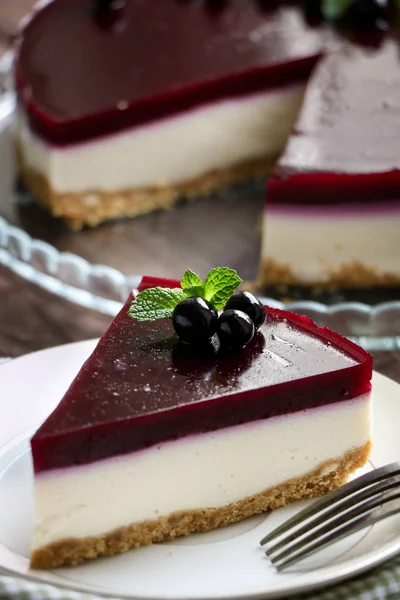 Tasty cheesecake with layer of black currant on a glass dish, mint leaves and currant berries.a bowl with berries and a vintage spoon,a small white jug with mint branches on the brown  table close up — Stock Photo, Image