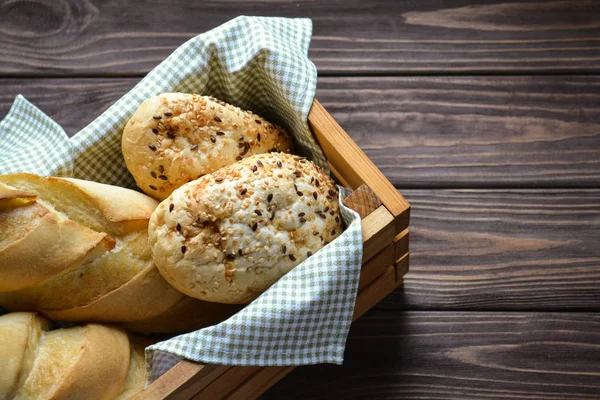 wooden crate box with two hot buns and two loaf inside, at the brown wooden table with green textile napkin under bread