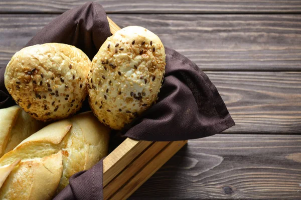 Houten krat doos met twee hete broodjes en twee brood binnen, aan de bruin houten tafel met bruin textiel servet onder brood — Stockfoto