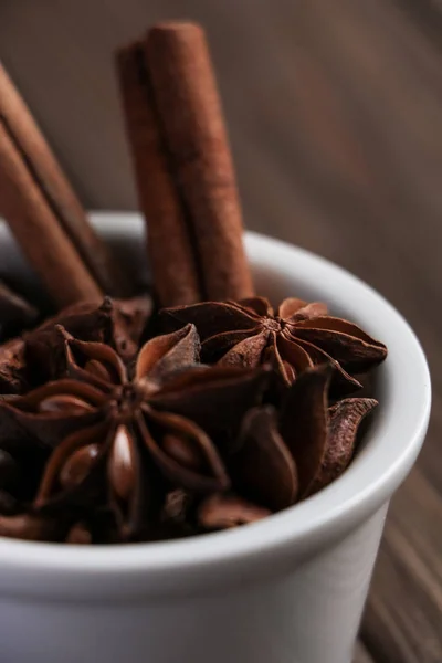 iki tarçın çubuğu, anason yıldız ve kahve çekirdekleri bir beyaz seramik kase kahverengi ahşap masa, lezzetli kahve veya mulled şarap için malzemeler