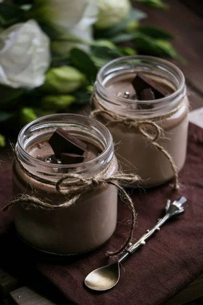 ip, tekstil peçete üzerinde bir vintage kaşık ile iki kavanoz lezzetli çikolata pannacotta tatlı bir vintage ahşap tepsi, kahverengi ahşap zemin üzerine koyu çikolata, beyaz çiçekler dilimleri ile bağlı