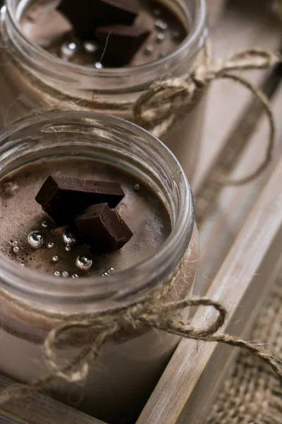 iki kavanoz lezzetli çikolata pannacotta tatlı yakın çekim bir vintage ahşap tepsi, koyu çikolata, dilimleri ile ip, tekstil peçete üzerinde bir vintage kaşık ile bağlı bir kahverengi ahşap zemin üzerinde beyaz çiçekler