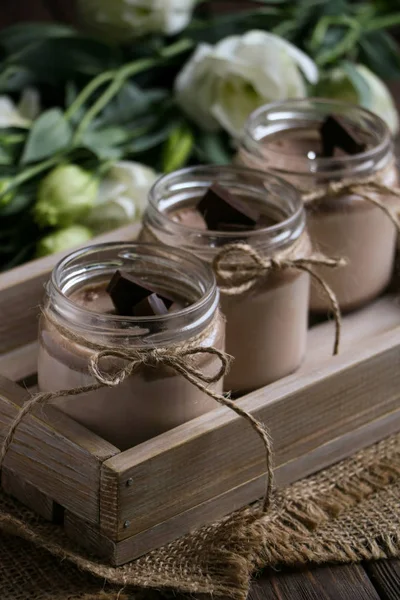 ip, tekstil peçete üzerinde bir vintage kaşık ile iki kavanoz lezzetli çikolata pannacotta tatlı bir vintage ahşap tepsi, kahverengi ahşap zemin üzerine koyu çikolata, beyaz çiçekler dilimleri ile bağlı