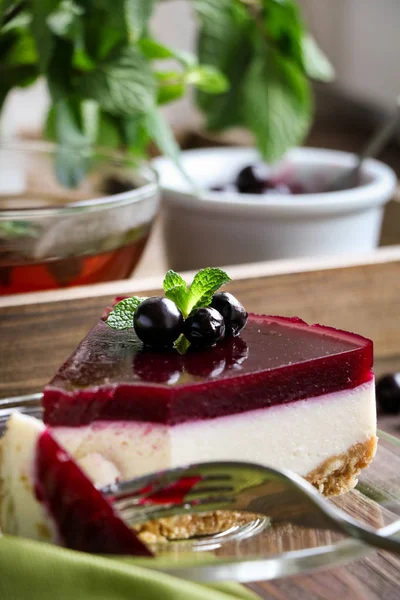 Delicious and homemade cheesecake with layer of black currant on a glass dish, mint leaves and currant berries.a bowl with berries and a vintage spoon,a small white jug with mint branches on the table Stockafbeelding
