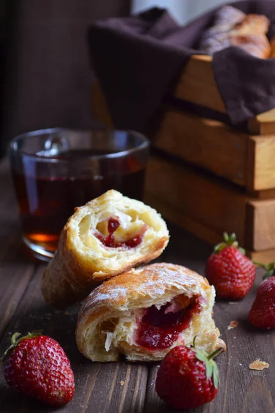 Aardbei croissants en een kopje zwarte thee in de buurt van het vak houten kist op de bruin houten tafel en vier aardbeien Rechtenvrije Stockfoto's