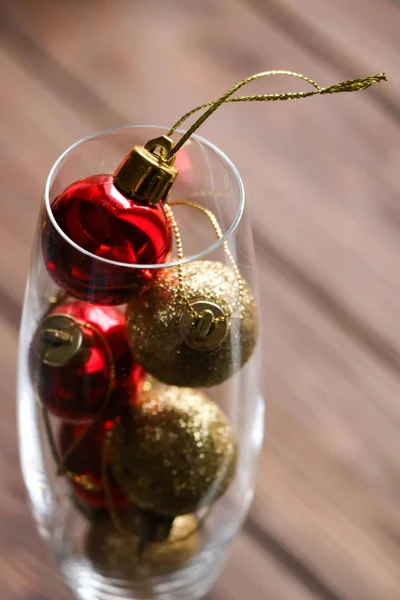 Kleine rode en gouden Kerstmis speelgoed voor de decoreren kerstboom binnen glas voor champagne op een bruin houten achtergrond, kerst en Nieuwjaar eve, kruiden vakantie Stockfoto