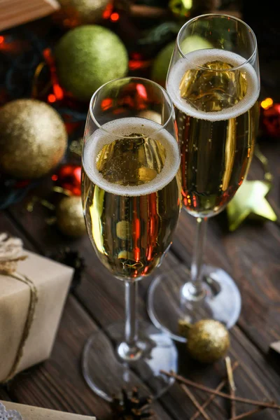 Two glasses of delicious champagne close up on a brown wooden background, christmas toys of red, green and gold color, gifts in craft paper Stockfoto
