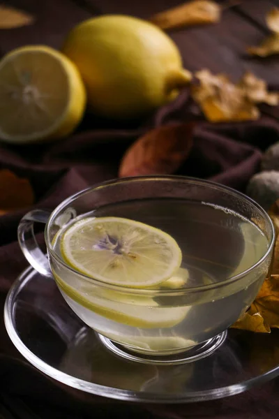 Een glas kopje nuttig hete thee met citroen en kruidige gember, die tegen griep beschermt en koude, droge Herfstbladeren op het textiel bruin servet op bruin houten tafel close-up Stockfoto