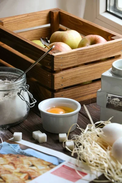 Ingrediënten voor een appeltaart op de keuken venster, bruin houten kist met appels, suiker, jar van bloem en recept Stockfoto