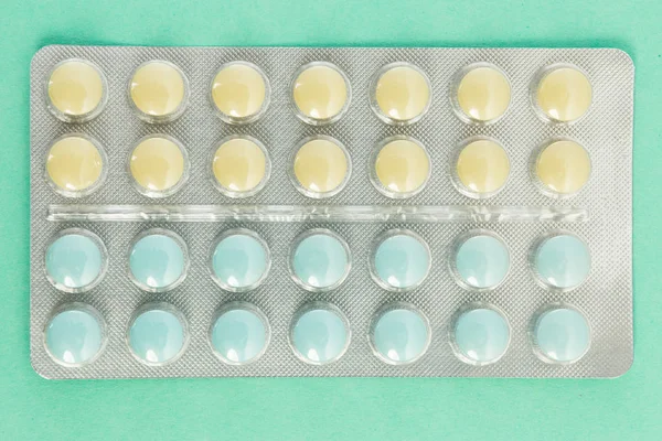 Un blister di pillole blu e gialle sulla tavola verde — Foto Stock