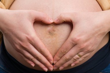 Hamile kadının karnına mükemmel kalp şeklinde yakın plan. Gelecekteki anne konsepti gibi.