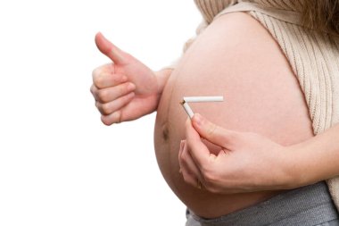 Hamile kadının baş parmak hareketi yaptığı ve beyaz arka planda izole edilmiş kırık sigara tuttuğu yakın plan.