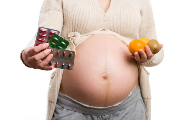对持有药物和水果作为选择概念的孕妇进行特写 将其隔离在白人背景下 — 图库照片