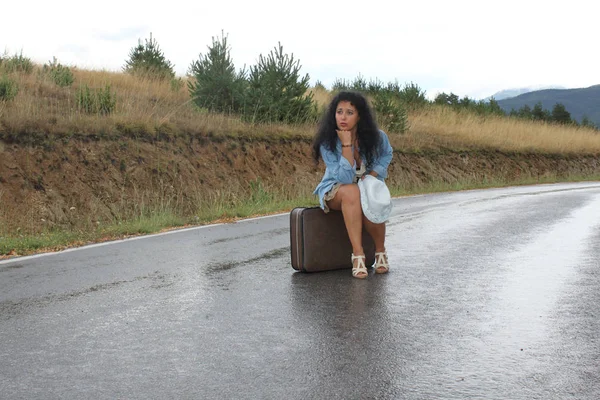 Una joven está sentada en una maleta. —  Fotos de Stock