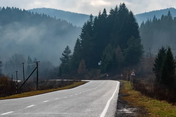 Dağ yolu boyunca giden bir araba var. Yüksek dağların tepeleri bulutlarla gizlidir. Sis. Sonbahar manzarası. Panoramik görünüm.