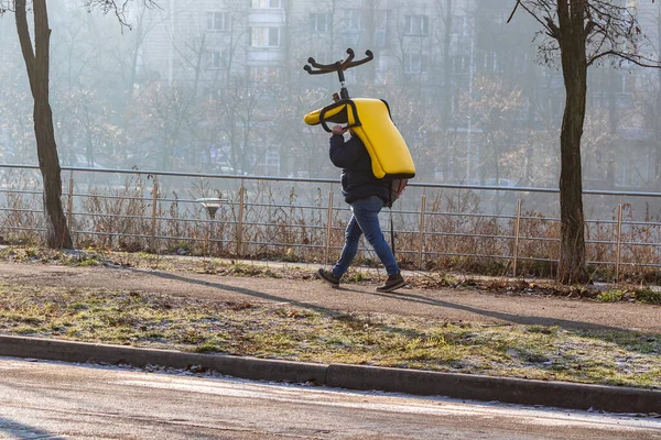 一大早 一个背着背包的年轻人头上拿着一把大的办公椅 冬雾中明亮的黄色扶手椅 一个大城市的街道 Kyiv Rusanivka — 图库照片