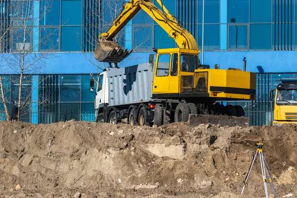 İnşaat alanındaki toprak işlerinde kazıcı yükleyici ve çöp kamyonu. Araziyi ağır bir kamyonun arkasına yüklüyorlar. Kazıcı yeni park alanı inşaatı için arazi kazıyor.