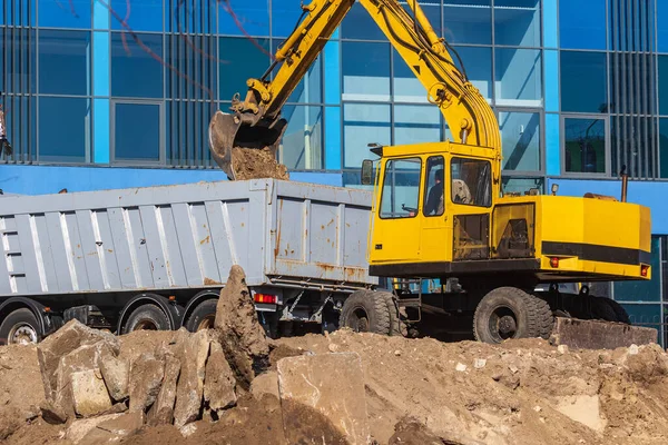 İnşaat alanındaki toprak işlerinde kazıcı yükleyici ve çöp kamyonu. Araziyi ağır bir kamyonun arkasına yüklüyorlar. Kazıcı yeni park alanı inşaatı için arazi kazıyor.