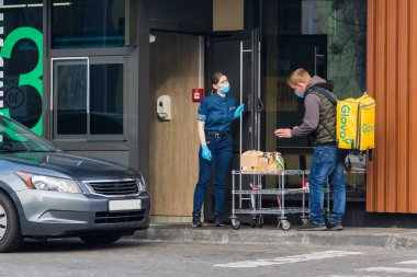 Kyiv Ukrayna - 10 Nisan 2020: Koruyucu maskeli ve koruyucu eldivenli işçiler bir fast food restoranındaki dağıtım hizmeti temsilcisine siparişleri ilettiler. Büyük şehirlerde karantina.