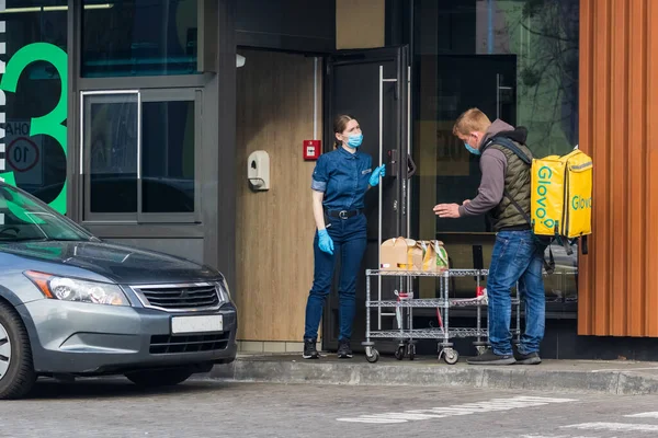Kyiv Ukrayna - 10 Nisan 2020: Koruyucu maskeli ve koruyucu eldivenli işçiler bir fast food restoranındaki dağıtım hizmeti temsilcisine siparişleri ilettiler. Büyük şehirlerde karantina.