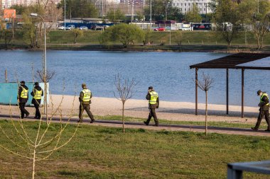 Kyiv Ukrayna - 17 Nisan 2020: Dünya koronavirüsü salgını. Koronavirüs nedeniyle karantina sırasında, polis memurları ve sağlık maskeli ulusal muhafız şehir parkında devriye geziyor..