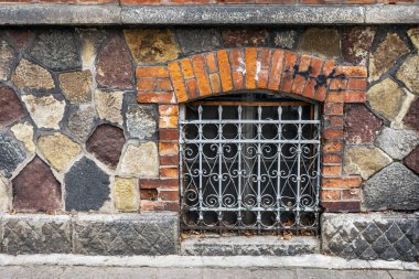 Eski evde işlenmiş demir ızgaralı pencere. Pencerenin önündeki tuğla duvar ve duvar süslemeli ızgara. 