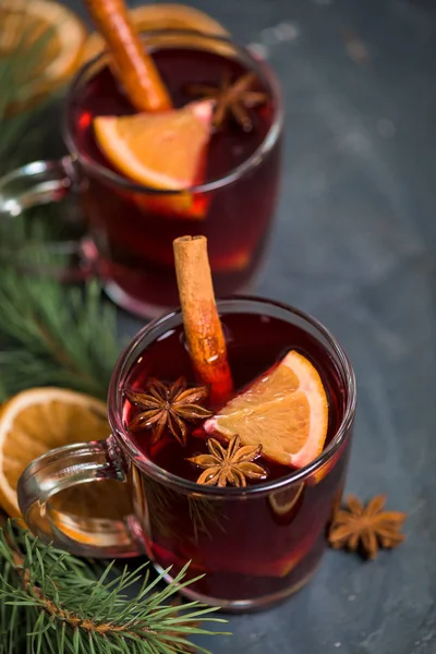 Vino caliente de invierno con especias alcohólicas a base de vino tinto, especias y naranja. sobre un fondo oscuro con ramas de abeto, rodajas de naranja. primer plano, espacio para el texto. la vista desde la parte superior —  Fotos de Stock