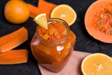 Kabak ve portakal reçeli karanlık bir arka planda cam bir kavanozda. Düzgün beslenme. Reçel kavanozunun arka planında portakal parçaları var. Kapat..