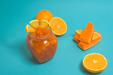 Taze besleyici portakal reçeli, balkabağı dilimleri ve portakal dilimleri, düzgün beslenmiş sağlıklı kahvaltı. Mavi arka planda cam bir kavanozda reçel. Metin için boşluk