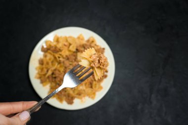 Esmer arka planda etli makarna. Kelebek şeklinde bir makarna çatalının üzerinde.