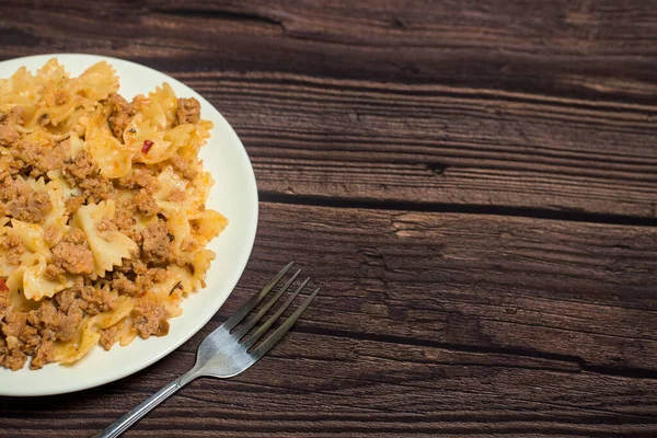 pasta with meat on a wooden background with a fork in hand. photo for banner, place for text