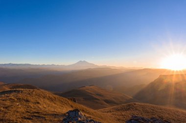 Gün batımında Ufukta Elbrus Dağı, güneş tarafından aydınlatılır. Dağ manzarasının manzarası.